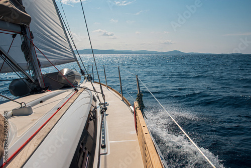 Deck, Segel und Reling einer Segelyacht mit Wellengang, Gischt und Bergen im Hintergrund im Mittelmehr © Felix