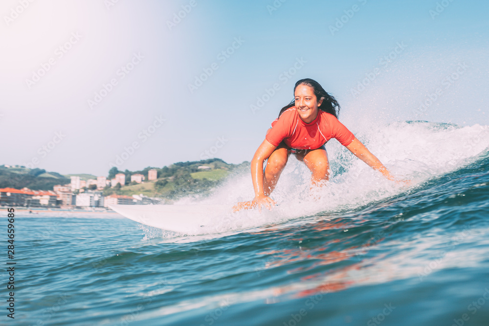 smiling teenager surfing, photographed from the water, on a sunny day with the green mountains in the background