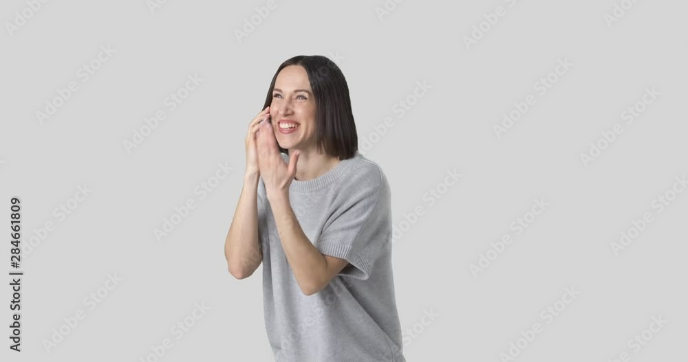 Excited young woman laughing while talking on mobile phone over white background Excited young woman laughing while talking on mobile phone over white background