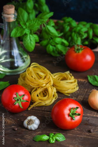 fresh tomatoes basil garlic olive oil glass bottle raw pasta fettuccine on wooden background vertical close up
