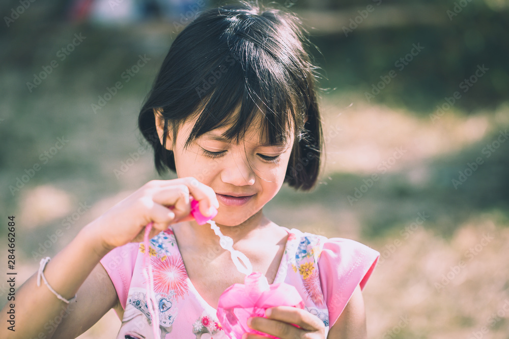 Cute little Asian girl playing soap bubbles at park, outdoors Cute little Asian girl playing soap bubbles at park, outdoors