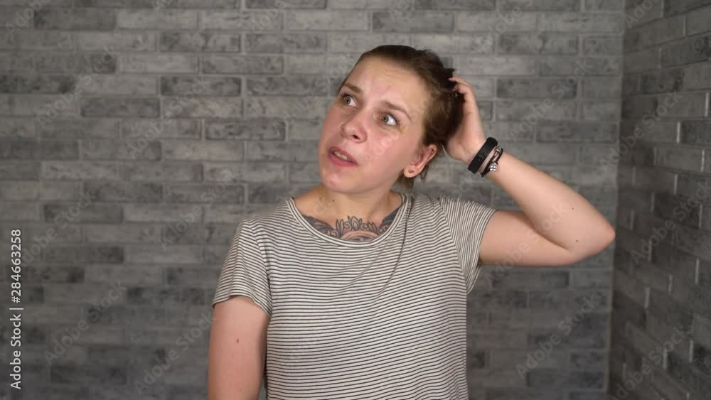 A woman with a tattoo scratching her head trying to remember something. The woman thinks or thought A woman with a tattoo scratching her head trying to remember something. The woman thinks or thought