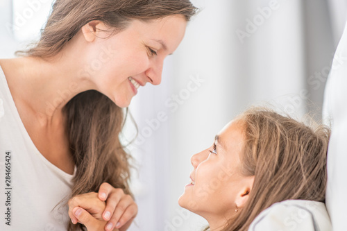 Happy mother talking with her little girl before bedtime at home