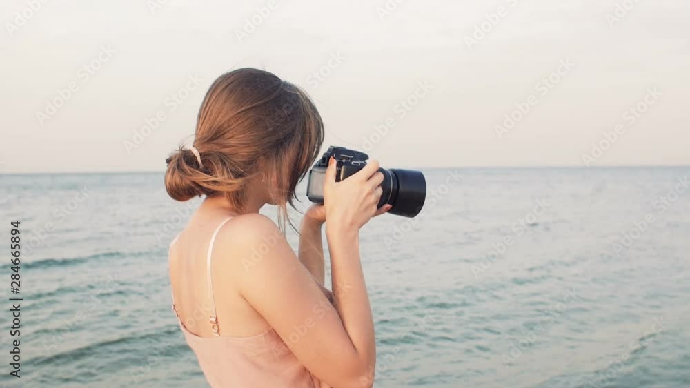 young woman photographer walks along the seashore and makes shots, the girl is engaged in a hobby on vacation at sunset, the concept of creative work young woman photographer walks along the seashore and makes shots, the girl is engaged in a hobby on vacation at sunset, the concept of creative work