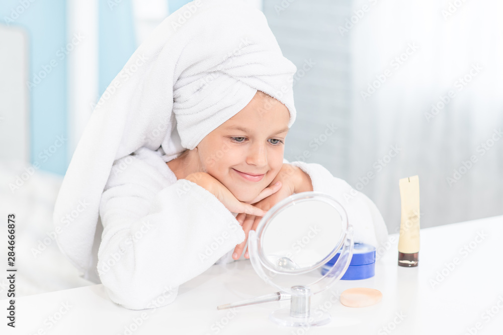 Happy little girl with a towel on her head looks in the mirror Happy little girl with a towel on her head looks in the mirror