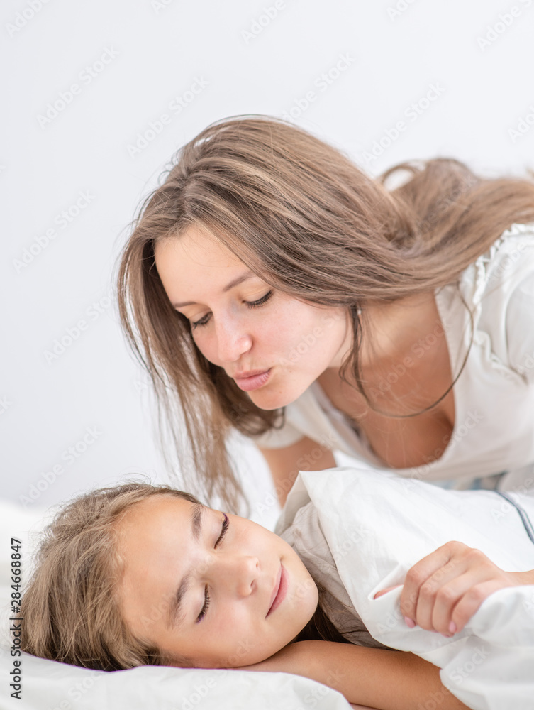 Happy mother wakes up a happy daughter with a kiss Happy mother wakes up a happy daughter with a kiss