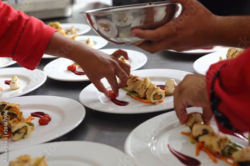 The hands of chefs prepare various dishes for a banquet that includes roasted chicken fillet and dessert.