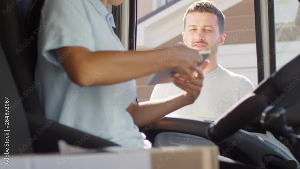 Handheld mid-section shot of unrecognizable female courier sitting in mail van and delivering package to man. She is asking client to sign receipt, then giving him box Handheld mid-section shot of unrecognizable female courier sitting in mail van and delivering package to man. She is asking client to sign receipt, then giving him box