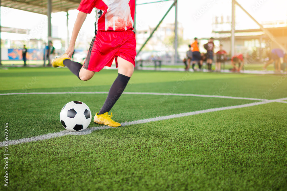 kid soccer player speed run to shoot ball to goal on artificial turf with blurry soccer player background. Soccer player training in football academy.