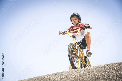 Young cyclist with bmx ready to start. Trendy young boy wearing helmet riding a bicycle looking the race track. Child having fun outdoor in the park. Safety, competition, youth, brave, sport, concept
