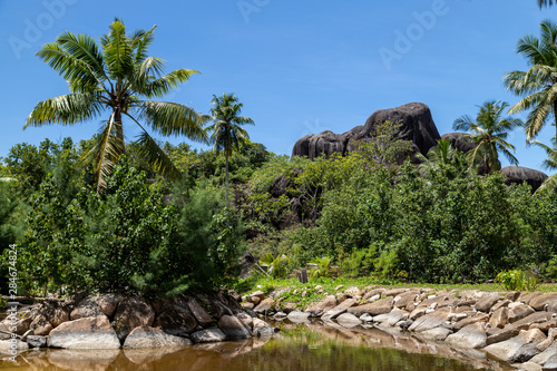 Landscape on Seychelles island La Digue with plam tree, granite rock in the background and water in front