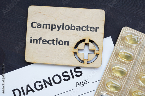 Text sign showing Campylobacter infection. The text is written on a small wooden board with red cross silhouette. There are pills ,diagnosis, blister,table on the photo. photo