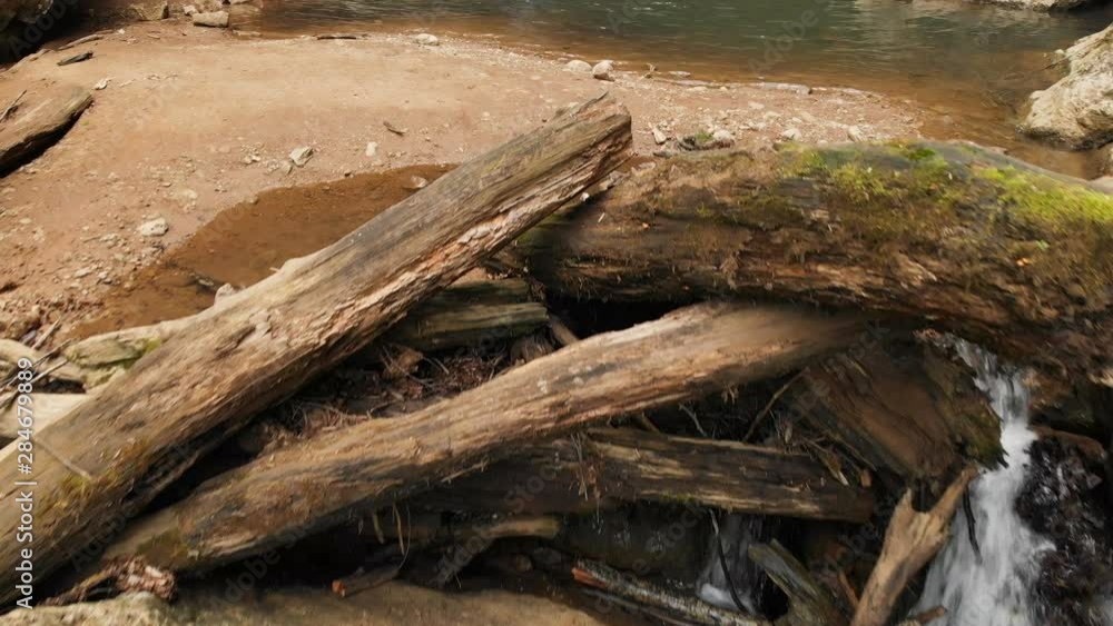 Close-up aerial view of a small water cascade among large stones and dry old logs in a summer forest. Forest cool wildlife concept Close-up aerial view of a small water cascade among large stones and dry old logs in a summer forest. Forest cool wildlife concept