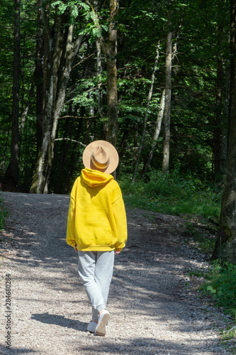 A girl in a bright yellow hoodie with a hat is walking along a path in the forest. © Chetgal 