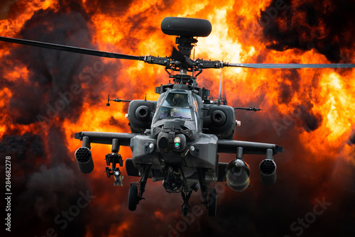 A AH-64 Apache attack helicopter in front of a large explosion.