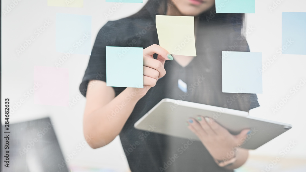 Obraz premium Woman holding sticky note and holding digital tablet on windows glass.