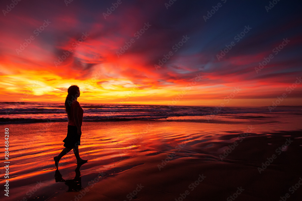 woman walking alone on the beach in the sunset