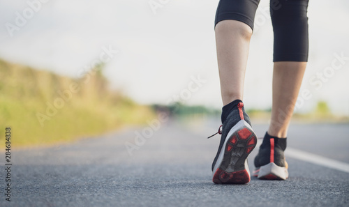 Runner feet running on road closeup on shoe. Woman fitness sunrise jog workout wellness concept. Young fitness woman runner athlete running at road