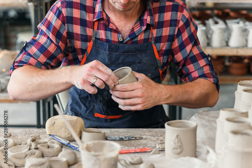 A middle-aged man in a work uniform make a clay shape of cup in a large creative pottery workshop. photo