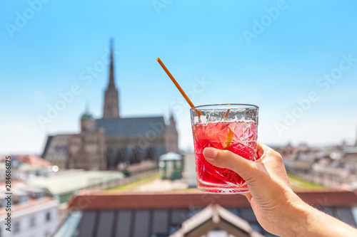 Photography Hand with glass of cocktail with Vienna cityscape view at the background