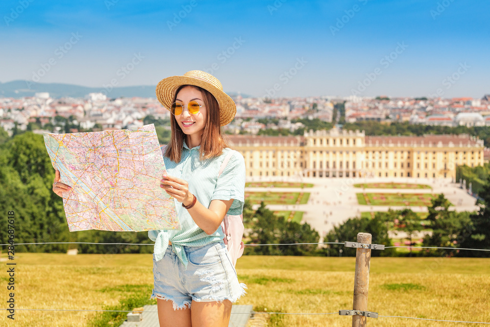 20 July 2019, Vienna, Austria: Happy young asian woman travel in Schoenbrunn royal palace garden. Searching right location on tourist map