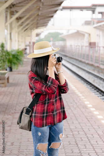 A pretty young woman traveler having fun traveling and taking photo at railway station in evening with vintage camera . The traveling photographer takes photo with old vintage camera at train station. © EduLife Photos