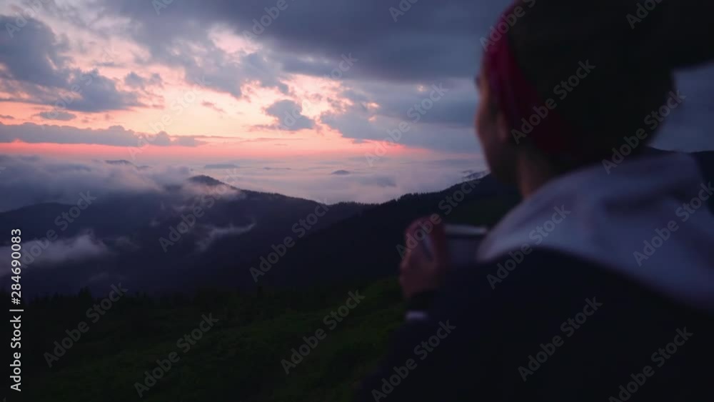 Over the shoulder view inspired young woman enjoying summer landscape at sunset. Close-up cheerful girl drinking mug tea enjoying scenic highland from the mountain top. Over the shoulder view inspired young woman enjoying summer landscape at sunset. Close-up cheerful girl drinking mug tea enjoying scenic highland from the mountain top.