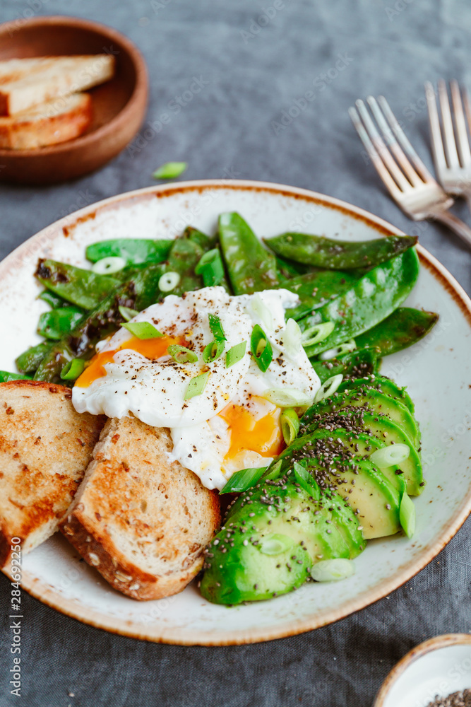 Healthy breakfast or lunch. Fried snow peas, avocado, poached eggs are sprinkled chia seeds with bread toasts. Healthy breakfast or lunch. Fried snow peas, avocado, poached eggs are sprinkled chia seeds with bread toasts.