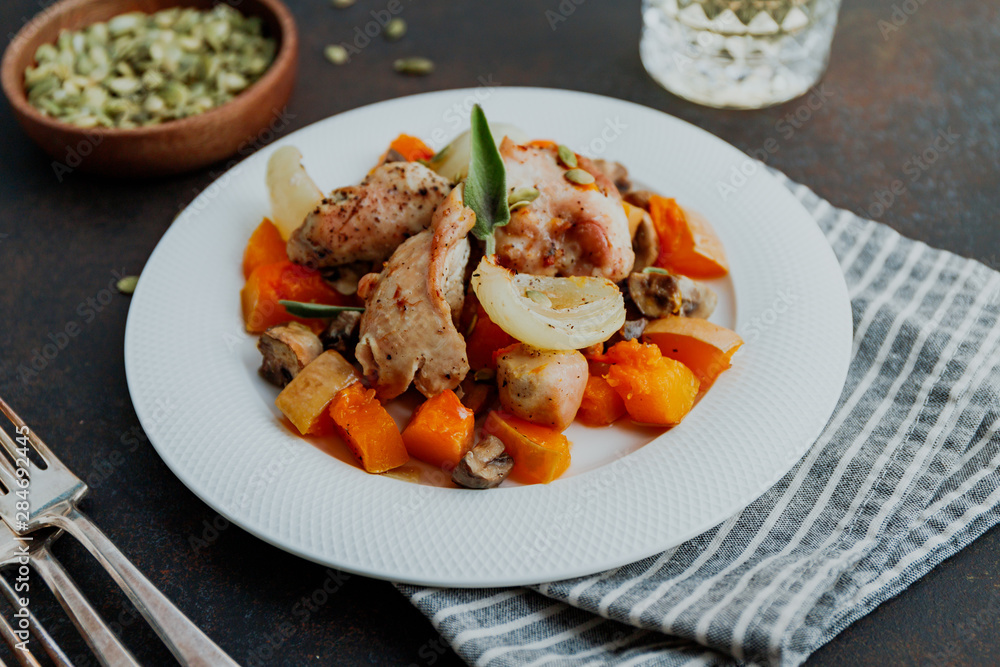 Seasonal autumn low calorie recipe from baked turkey medallions with pumpkin, onion, champignons and sage on a white plate.