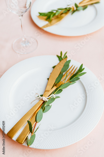 Festive table setting for celebrate event or family dinner with two plates and golden cutlery on a pink tablecloth.