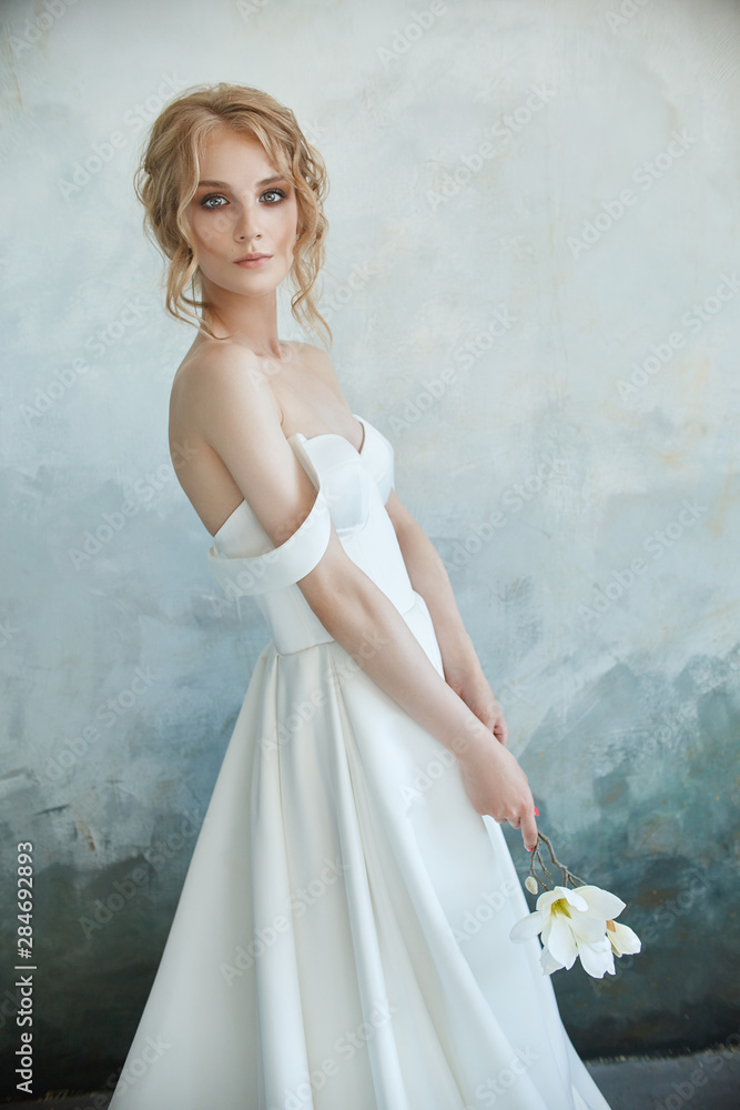 Girl in a chic long dress sitting on the floor. White wedding dress on the  bride's