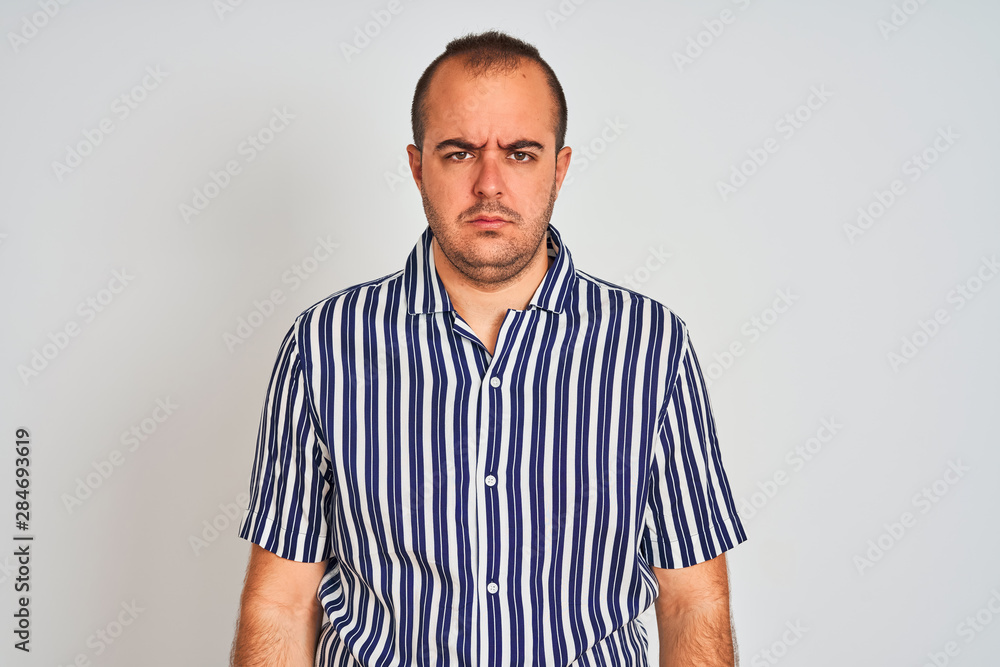 Young man wearing blue striped shirt standing over isolated white background skeptic and nervous, frowning upset because of problem. Negative person. Young man wearing blue striped shirt standing over isolated white background skeptic and nervous, frowning upset because of problem. Negative person.