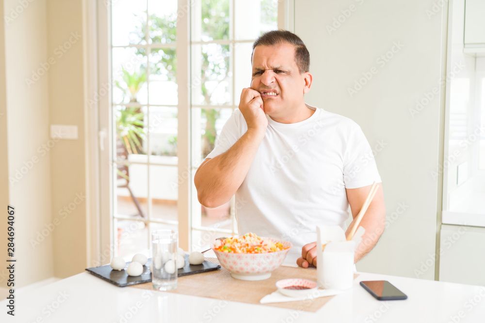 Middle age man eating asian food with chopsticks at home looking stressed and nervous with hands on mouth biting nails. Anxiety problem. Middle age man eating asian food with chopsticks at home looking stressed and nervous with hands on mouth biting nails. Anxiety problem.