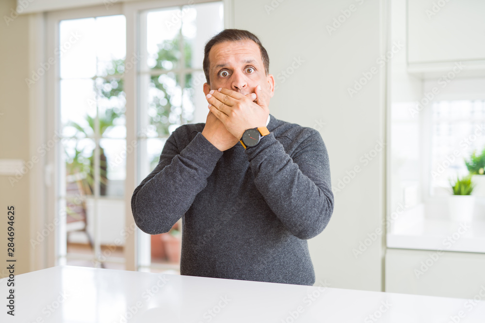 Middle age man sitting at home shocked covering mouth with hands for mistake. Secret concept. Middle age man sitting at home shocked covering mouth with hands for mistake. Secret concept.