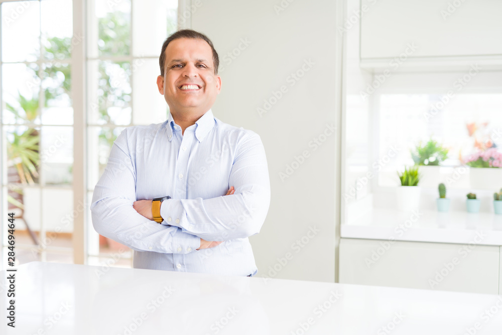 Middle age man sitting at home happy face smiling with crossed arms looking at the camera. Positive person.