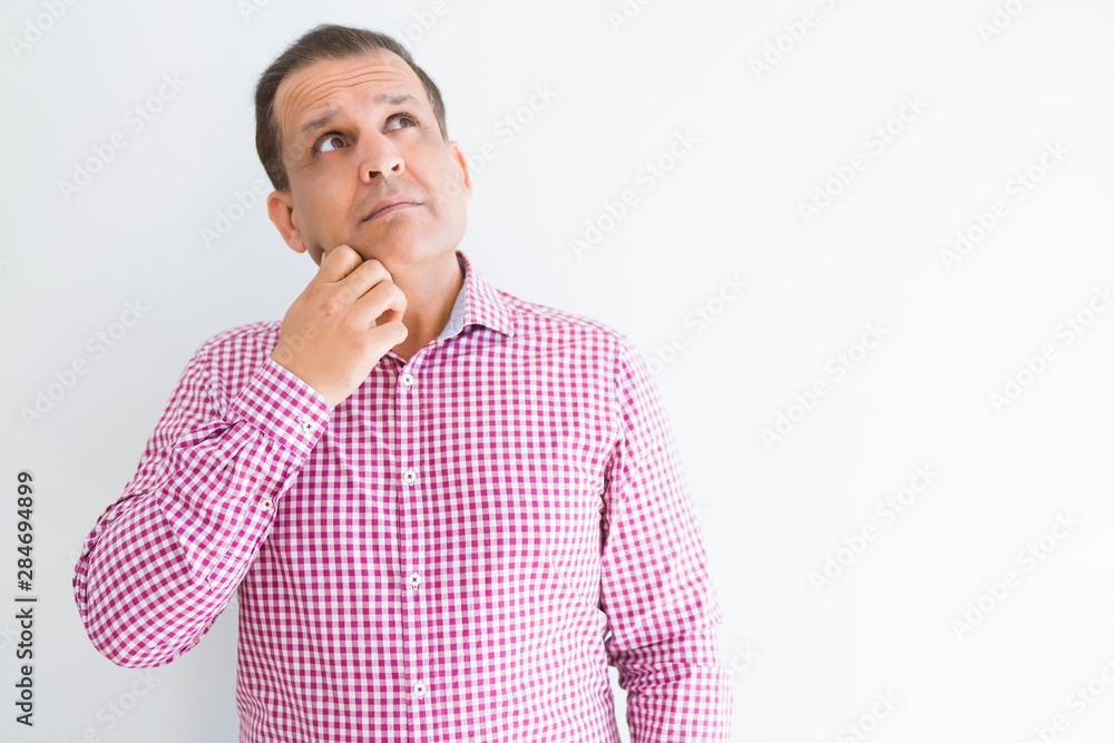 Middle age man wearing business shirt over white wall with hand on chin thinking about question, pensive expression. Smiling with thoughtful face. Doubt concept. Middle age man wearing business shirt over white wall with hand on chin thinking about question, pensive expression. Smiling with thoughtful face. Doubt concept.
