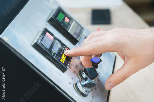 Close-up of a male hand on a dashboard controlling production equipment with buttons and displays in a locksmith's workshop for furniture production