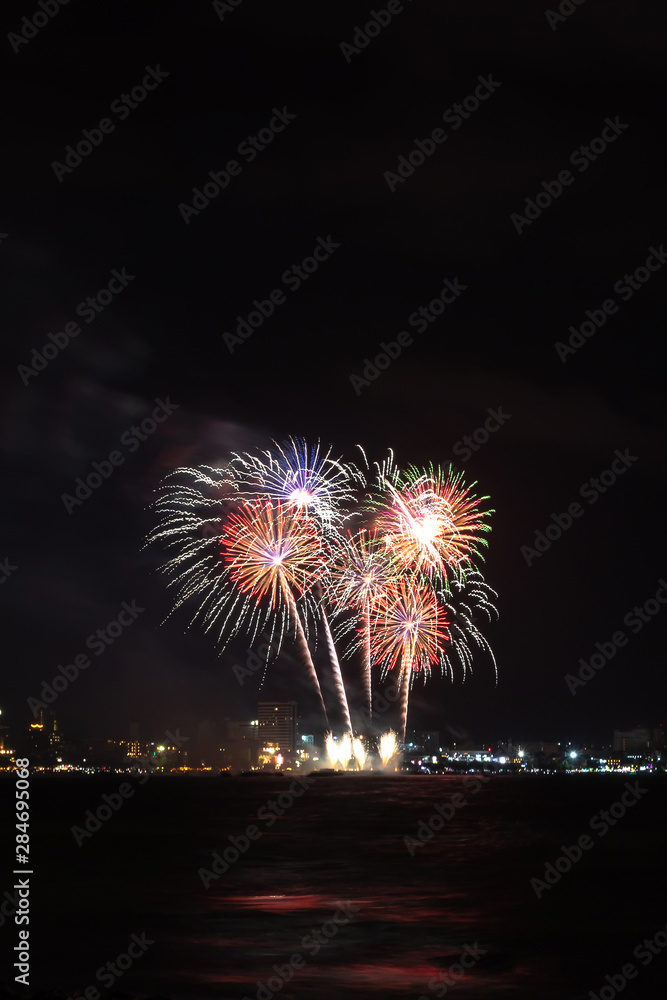 Fireworks over sea with city night on background. Festive colorful fireworks celebration in night sky.