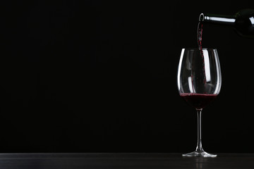 Pouring wine from bottle into glass on table against black background, space for text
