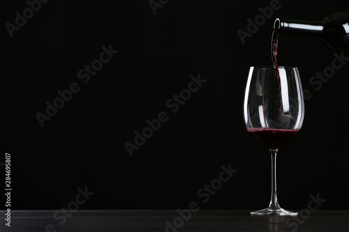 Pouring wine from bottle into glass on table against black background, space for text