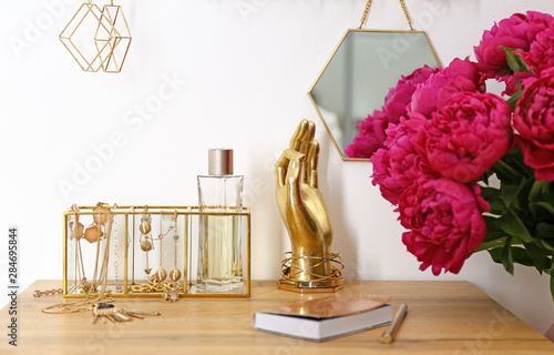 Fotografering Composition with gold accessories and flowers on dressing table near white wall