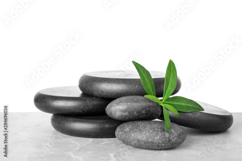 Pile of spa stones and green leaves on table against white background