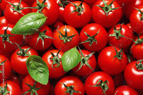 Delicious ripe cherry tomatoes and basil leaves as background, top view © New Africa