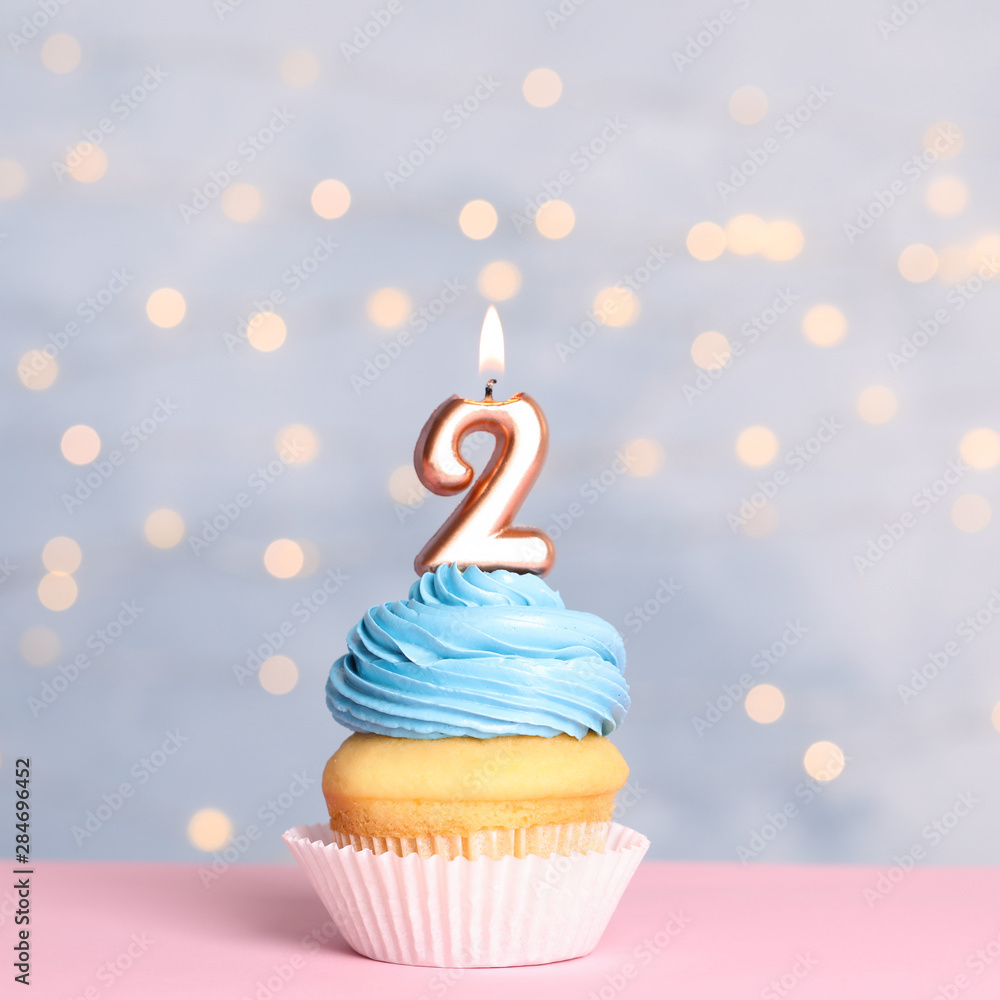 Birthday cupcake with number two candle on table against festive lights  Stock Photo | Adobe Stock