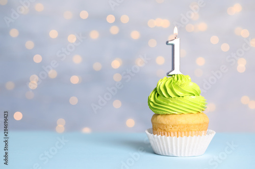 Birthday cupcake with number one candle on table against festive lights  space for text