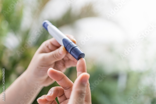 Close up of woman hands using lancet on finger to check blood sugar level by Glucose meter in the morning. Use as Medicine  diabetes  glycemia  health care and people concept.