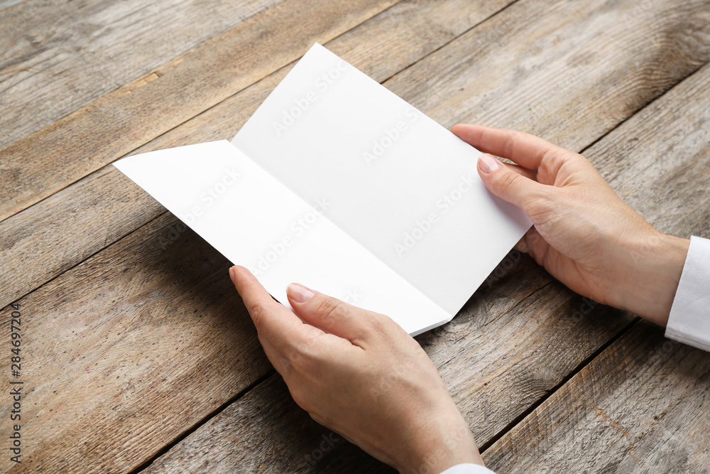 Young woman holding blank brochure at wooden table, closeup. Mock up for design Young woman holding blank brochure at wooden table, closeup. Mock up for design