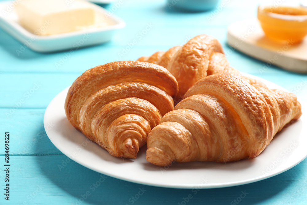 Plate with tasty croissants on light blue wooden table, closeup. French pastry