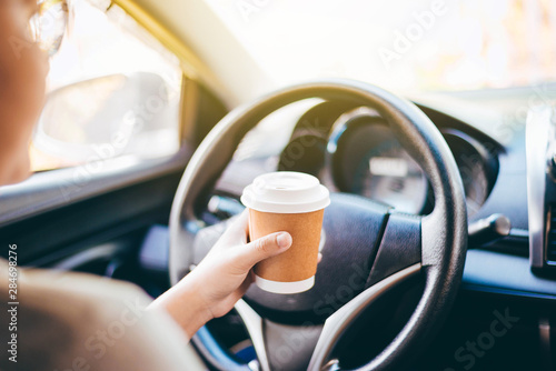 woman's hand holding a coffee cup to take away, she is driving in the morning.