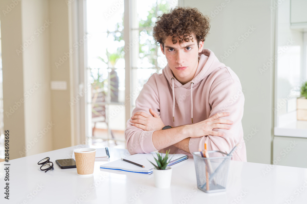 Young student man writing on notebook and studying skeptic and nervous, disapproving expression on face with crossed arms. Negative person. Young student man writing on notebook and studying skeptic and nervous, disapproving expression on face with crossed arms. Negative person.